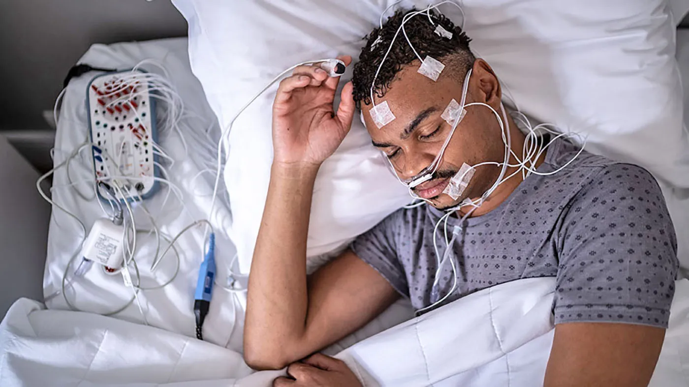 Picture of man undergoing a sleep study evaluation. It shows the equipment used to evaluated patients for sleep apnea.